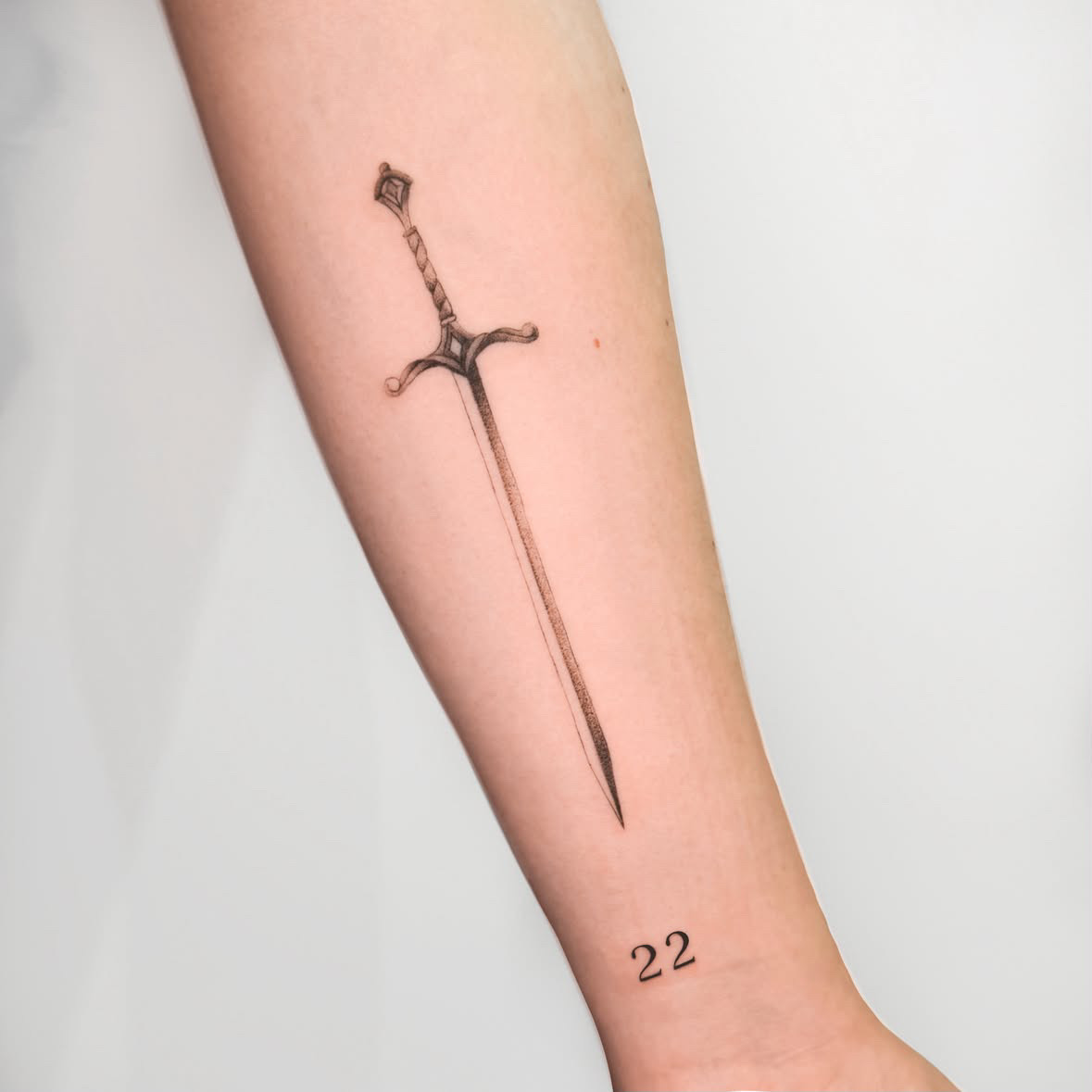 Schwert mit „22“ · Fine Line · Unterarm · Tattoo von Inna, Velvet Line Karlsruhe
