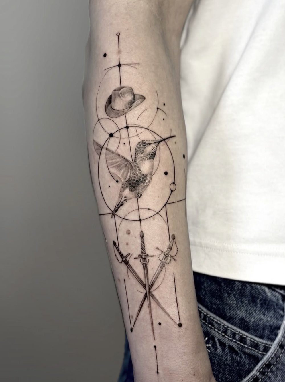 Kolibri mit Hut, Degen und geometrischen Linien am Unterarm, von Barni, Velvet Line Karlsruhe
